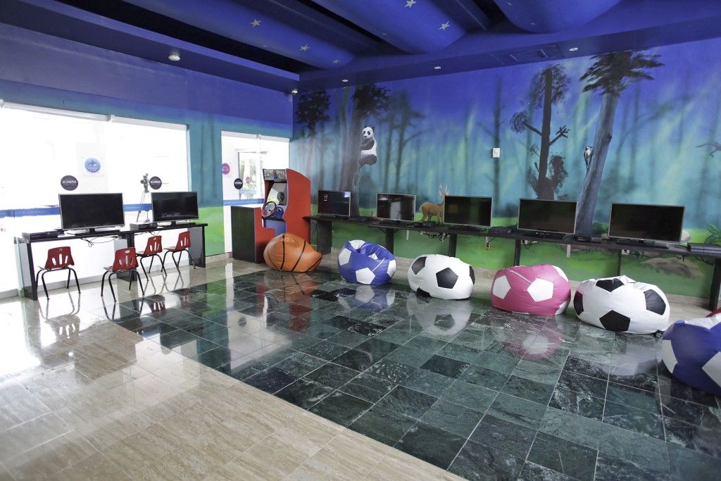 فندق غراند أويسيز بالم شامل كليًا كانكون المظهر الخارجي الصورة The photo shows a colorful indoor space designed for children, featuring a playful and vibrant atmosphere. The walls are decorated with a mural depicting a forest scene, while the ceiling is painted in a bold blue hue. 

In the room, there are severa
