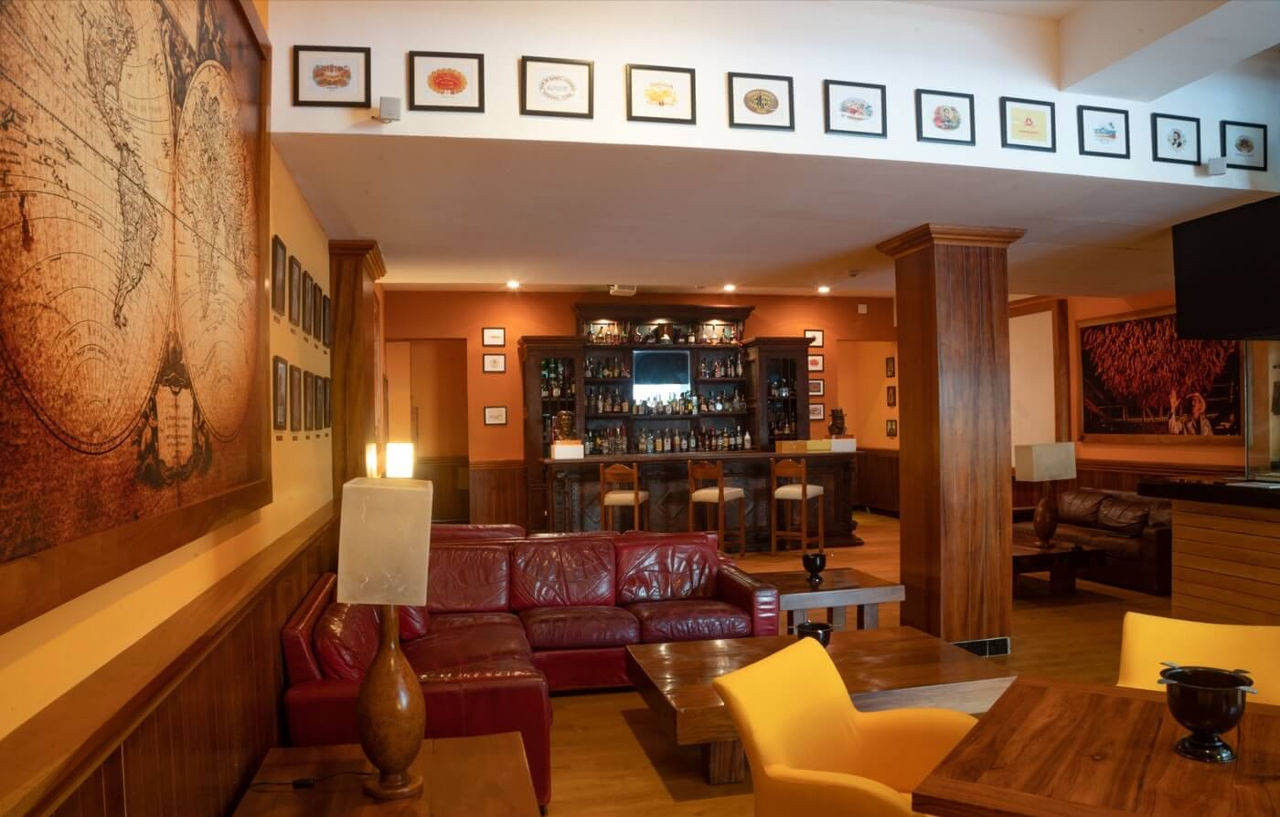فندق غراند أويسيز بالم شامل كليًا كانكون المظهر الخارجي الصورة The photo shows a cozy interior of a bar or lounge area. It features a comfortable setup with a deep red leather sofa and wooden tables. The walls are adorned with decorative artwork, including various framed pictures that add character to the space.